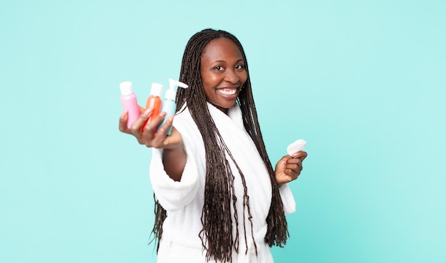 Black african american adult woman wearing bathrobe and holding cosmetic products