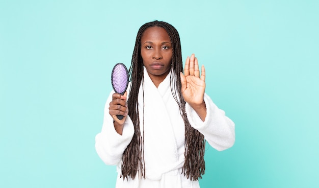 Black african american adult woman wearing a bathrobe and holding a hair brush