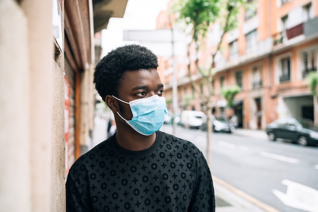 Black african american boy walking down the street with a blue face mask protecting himself from the covid-19 coronavirus pandemic
