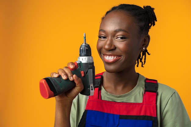 Black african american female model in uniform holding a screwdriver repair tool against yellow back