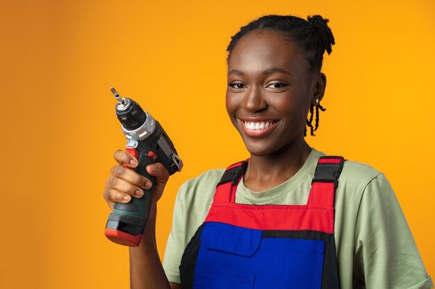 Black african american female model in uniform holding a screwdriver repair tool against yellow back