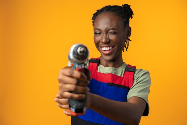 Black African American female model in uniform holding a screwdriver repair tool against yellow background