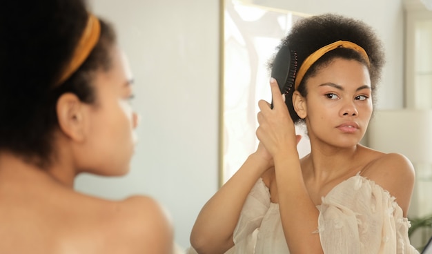 Black african american woman combing her hair with hairbrush makes hairstyle