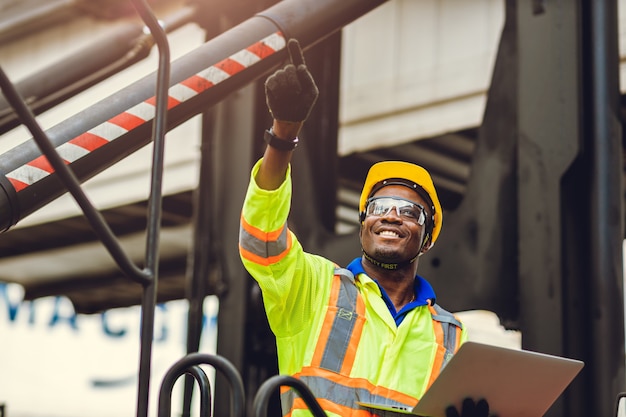 Black African American worker as staff foreman proud to happy smile working control loading cargo in shipping logistic warehouse with safety suit.