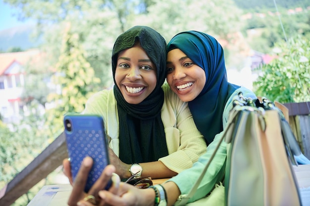 black african female friends using smart phone together wearing traditional islamic hijab clothes