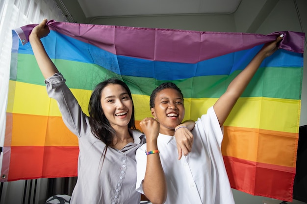 Black African LGBT woman holding LGBTQ rainbow flag with asian LGBT woman upside down new member of gay pride movement concept