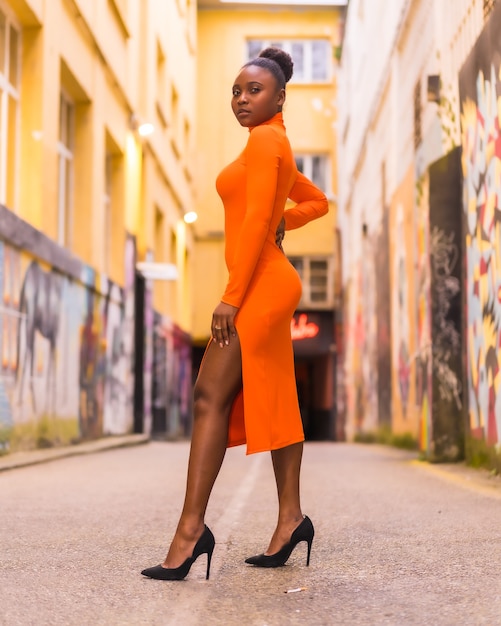 Black African woman in an orange dress and black heels on a city street