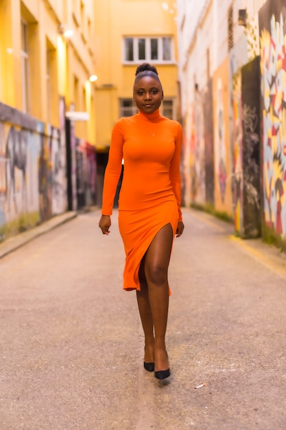 Black African woman in an orange dress and black heels on a city street