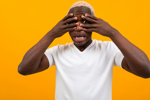 Black african young man cons his face with his hands on yellow