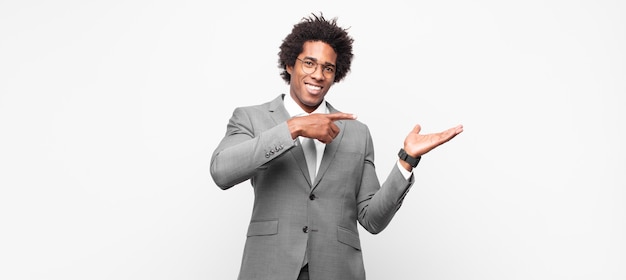 Black afro businessmansmiling cheerfully and pointing to copy space on palm on the side, showing or advertising an object