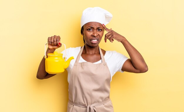 Black afro chef woman feeling confused and puzzled showing you are insane crazy or out of your mind teapot concept