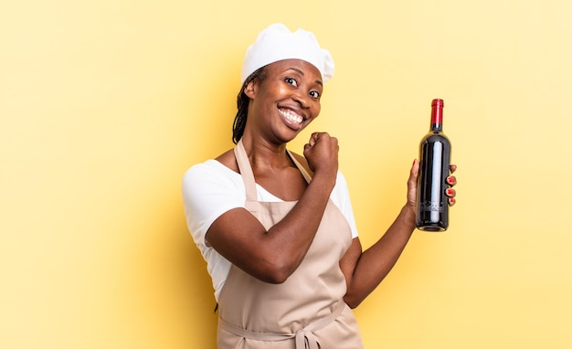 挑戦に直面したり、良い結果を祝ったりするときに幸せな前向きで成功した動機を感じている黒人のアフロシェフの女性ワインボトルのコンセプト