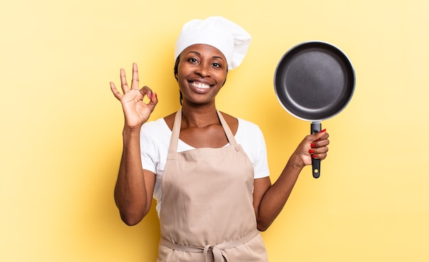 Черная афро-шеф-повар чувствует себя счастливой, расслабленной и удовлетворенной, демонстрирует одобрение жестом `` ОК '' и улыбается