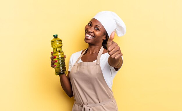 Black afro chef woman feeling proud, carefree, confident and happy, smiling positively with thumbs up. olive oil concept