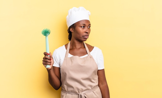 Black afro chef woman feeling sad, upset or angry and looking to the side with a negative attitude, frowning in disagreement. cleaning dishes concept