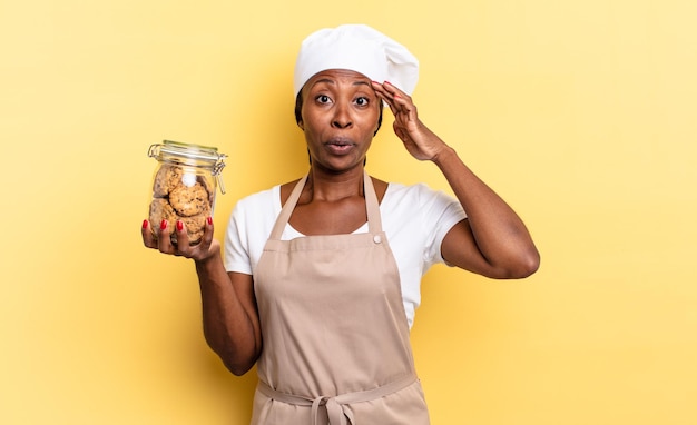 Black afro chef woman looking happy, astonished and surprised, smiling and realizing amazing and incredible good news. cookies concept