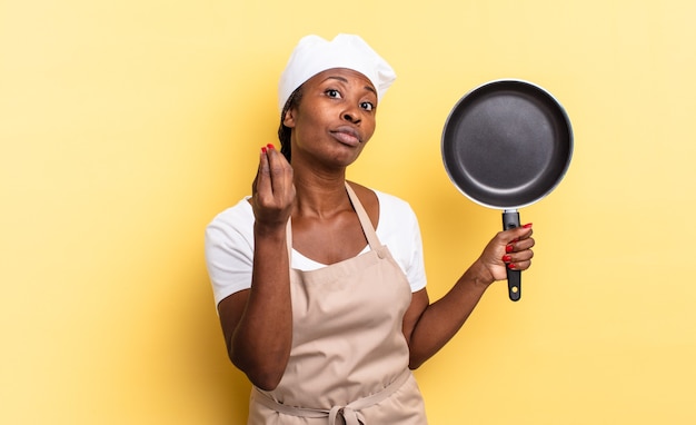 Black afro chef woman making capice or money gesture, telling you to pay your debts!