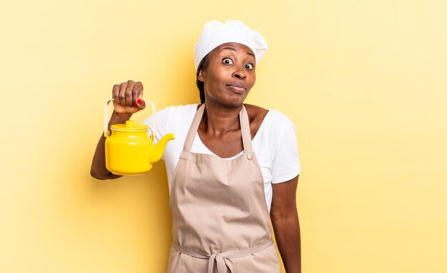 Black afro chef woman shrugging feeling confused and uncertain doubting with arms crossed and puzzled look teapot concept