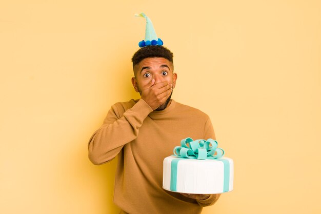 Black afro man covering mouth with hands with a shocked birthday concept