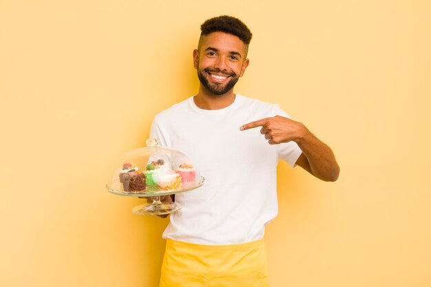 Uomo afro nero che sorride allegramente sentendosi felice e indicando il concetto di torte fatte in casa laterali