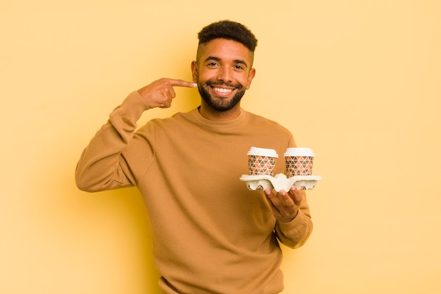 Black afro man smiling confidently pointing to own broad smile take away coffee concept