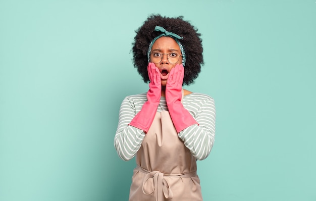 Black afro woman feeling shocked and scared, looking terrified with open mouth and hands on cheeks. housekeeping concept.. household concept