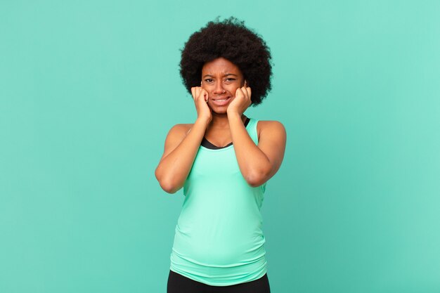 Black afro woman looking angry stressed and annoyed covering both ears to a deafening noise sound or loud music