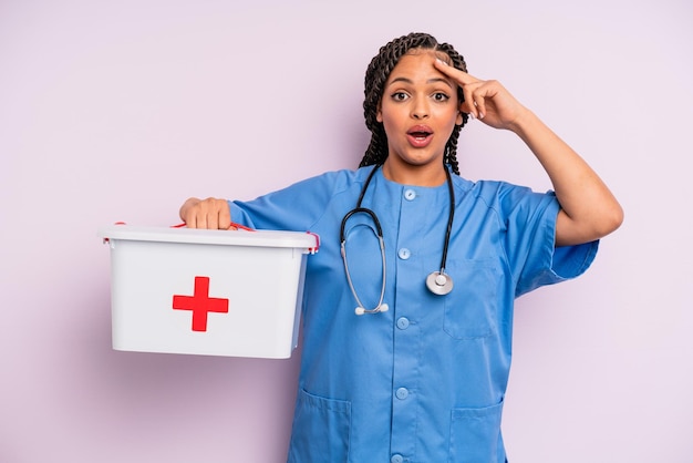 Black afro woman looking happy astonished and surprised nurse
and first aid kit concept