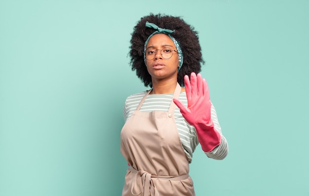 Black afro woman looking serious, stern, displeased and angry showing open palm making stop gesture. housekeeping concept. household concept