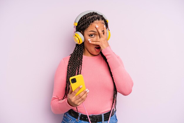 Black afro woman looking shocked, scared or terrified, covering face with hand. listening music concept