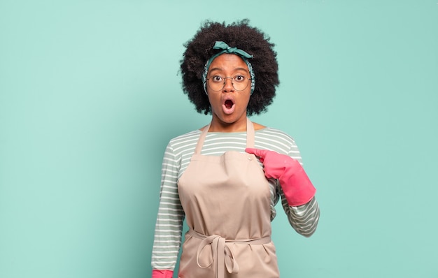 Donna afro nera che sembra scioccata e sorpresa con la bocca spalancata, che indica se stessa. concetto di pulizia.concetto domestico