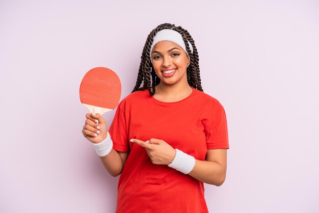 Black afro woman smiling cheerfully, feeling happy and pointing to the side. ping pong concept