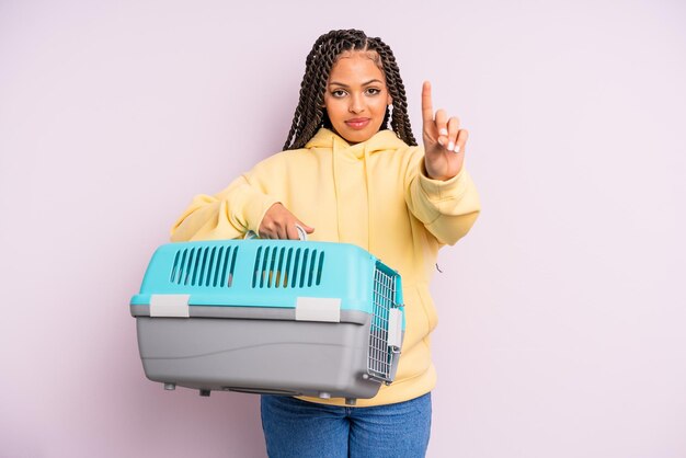 Black afro woman smiling and looking friendly, showing number one. pet travel container concept