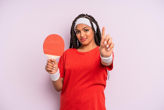 Black afro woman smiling and looking friendly showing number one ping pong concept