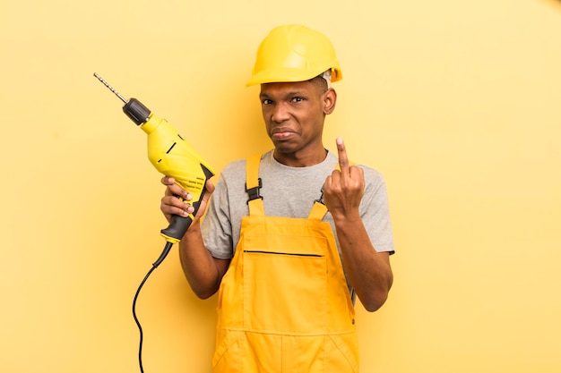 Black afro young man feeling angry annoyed rebellious and\
aggressive housekeeper worker with a drill