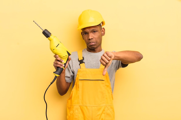 Black afro young man feeling crossshowing thumbs down housekeeper worker with a drill