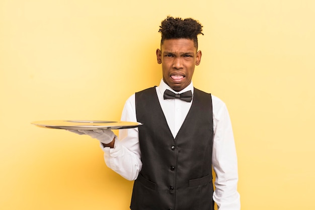 Black afro young man feeling disgusted and irritated and tongue out waiter concept with a tray