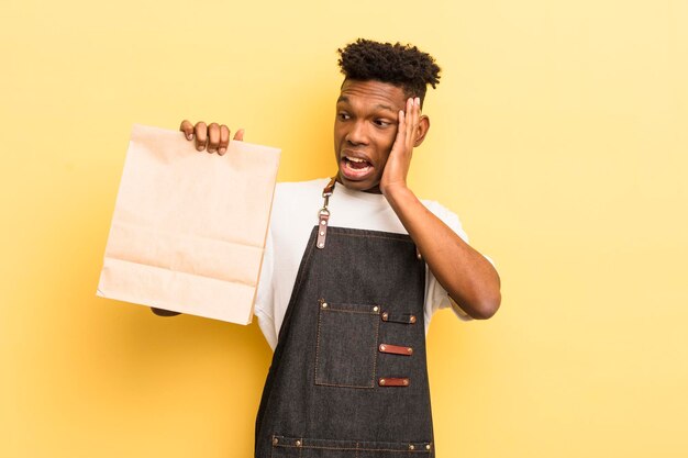 Black afro young man feeling happy excited and surprised take away food employee concept