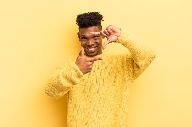 Black afro young man feeling happy friendly and positive smiling and making a portrait or photo frame with hands