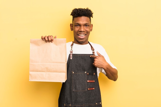 Black afro young man feeling happy and pointing to self with an excited take away food employee concept