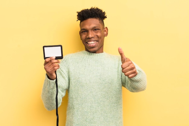 Black afro young man feeling proudsmiling positively with thumbs up accreditation pass id concept