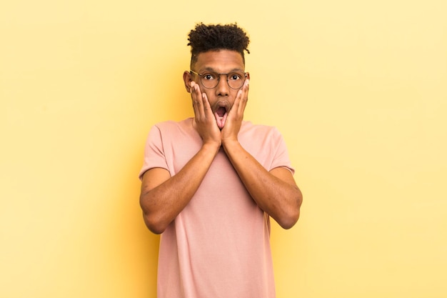 Black afro young man feeling shocked and scared looking terrified with open mouth and hands on cheeks