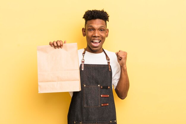ショックを受けた笑いと成功を祝う黒人のアフロの若い男は、食品従業員の概念を奪う