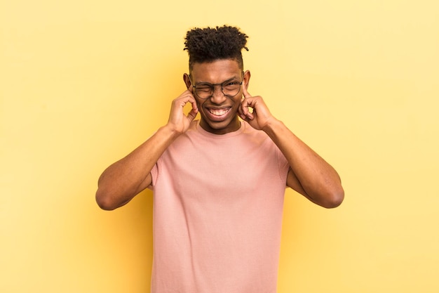 Black afro young man looking angry stressed and annoyed covering both ears to a deafening noise sound or loud music