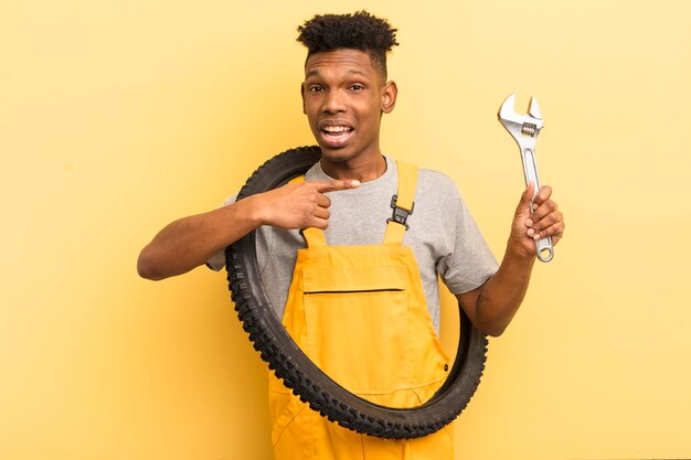 Black afro young man looking excited and surprised pointing to the side bycicle mechanic concept