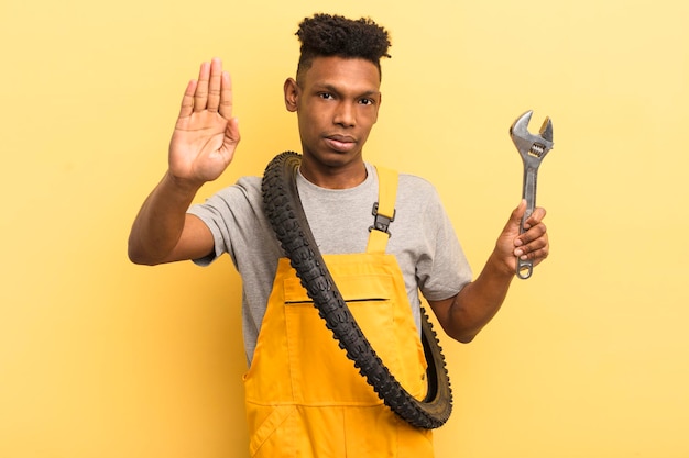 Black afro young man looking serious showing open palm making stop gesture bycicle mechanic concept