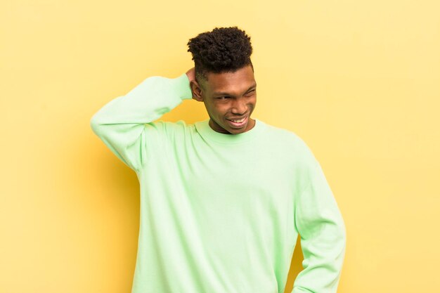 Black afro young man smiling cheerfully and casually taking hand to head with a positive happy and confident look