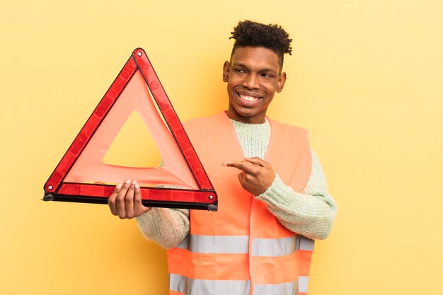 Black afro young man smiling cheerfully feeling happy and pointing to the side car fault and triangle concept