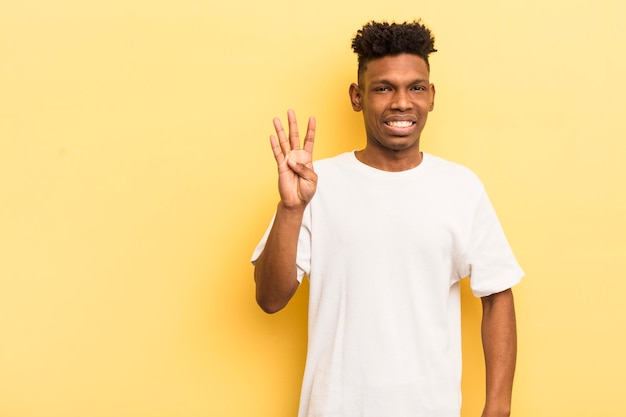 Black afro young man smiling and looking friendly showing number four with a copy space to the side