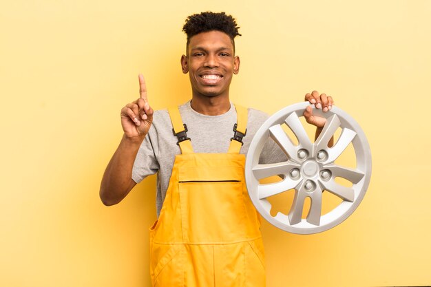 Black afro young man smiling and looking friendly showing number one car mechanic concept